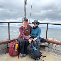 3. Rachel Black is seated next to Raina Joines with the ocean and mountains in the background.