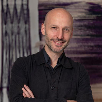 Glenn Adamson facing forward and smiling, wearing a black shirt, arms folded.