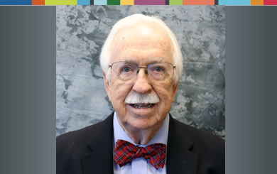 Jack is facing forward and smiling. He has white hair, a white mustache and wears glasses, a bow tie with a shirt and jacket.