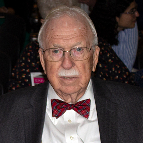 Jack Davis is facing forward. He wears glasses, a dark suit and a red bow tie.