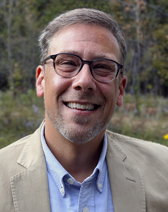 Dustin Garnet is facing forward and smiling. He has glasses and gray hair.