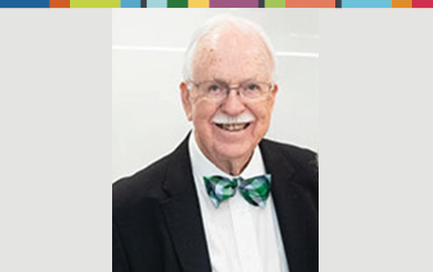 Jack is facing forwar and smiling. He has white hair, a white mustache and wears glasses, a bow tie with a shirt and jacket.