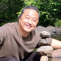 Jun Hu is facing forward and smiling while wearing a brown T-shirt.