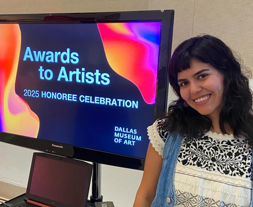 Vanessa is next to a monitor that shows the Dallas Museum of Art Honoree slide.