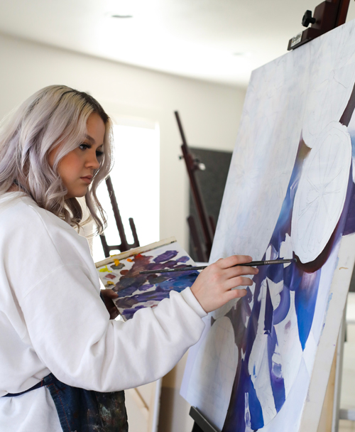 Allyson in a white top and apron painting on a canvas.