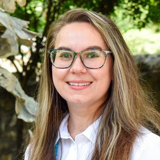 Marie-Claire is facing forward and smiling. She has long blonde hair and wears a white shirt.