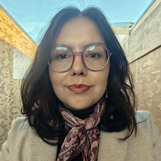 Marcela is facing forward. She has brown hair and wears glasses