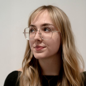 Rachel is looking to her right. She has long blonde hair and wears glasses.