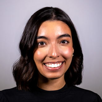 Isabella is facing forward and smiling. She has dark hair and wears a dark top.