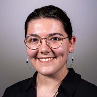 Isabella is facing forward and smiling. Her hair is pulled back and is wearing glasses.