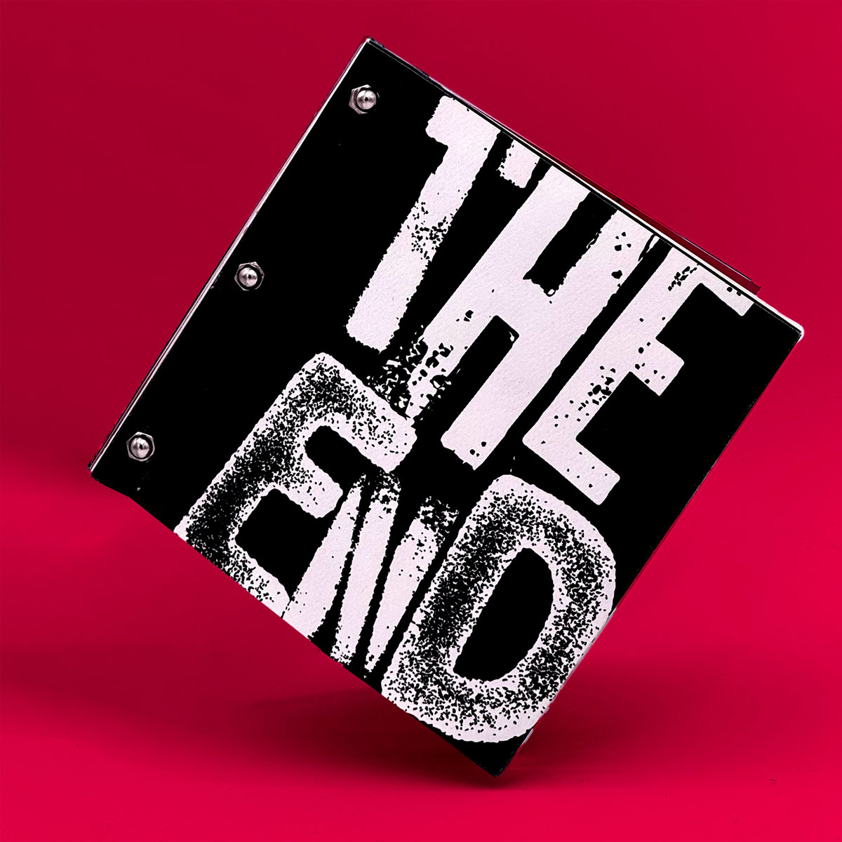 Photo of a square, black and white booklet. It's pages are bound by 3 silver bolts. The cover has a grunge and stencil-like font, and it reads "The End."