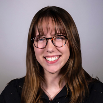 Samantha is facing forward and smiling. She has long brown hair and wears glasses.