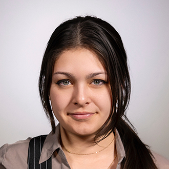 Kari is facing forward. She has brown hair and wears a beige top.
