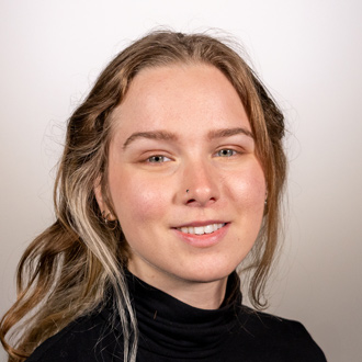 Ylliana is facing forward and smiling. She has blonde hair and wears a black top.