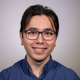 Jhan Le is facing forward and smiling. He has dark hair and wears glasses and a blue shirt.