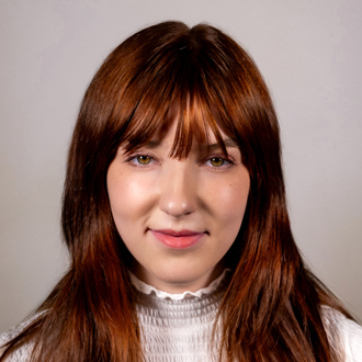 Zoey is facing forward. She has long red hair and wears a white blouse.