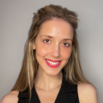 Tristan is facing forward and smiling. She has long blonde hair and wears a sleeveless shirt.