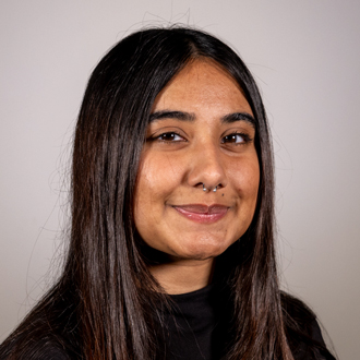 Prarthana is facing forward and smiling. She has dark hair and wears a dark shirt.