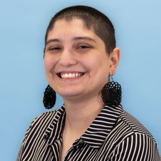 Arianna is facing forward and smiling. She has short hair and wears pendulous earrings.