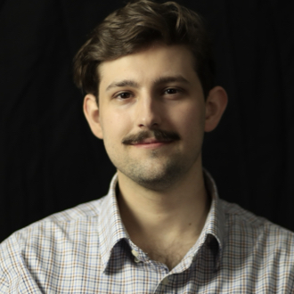 Duncan is facing forward and smiling. He has short dark hair and a mustache.