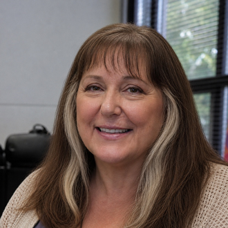 Ruth is facing forward and smiling. She has long brown hair with bangs.