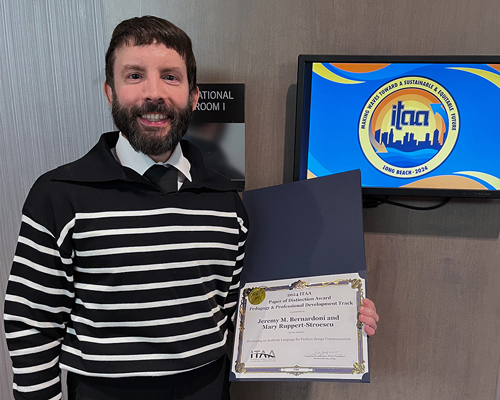 Jeremy in a black sweater next to a digital sign of the ITAA conference logo.