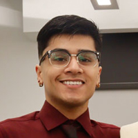 Johnathan De la Cruz smiling, standing next to a dress he designed