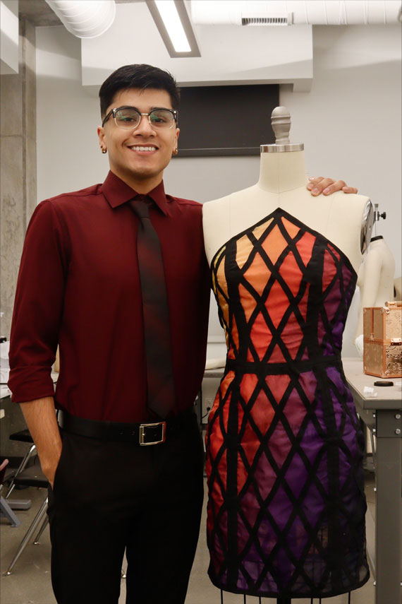 Johnathan is facing forward and smiling. He is standing next to a mannequin wearing one of his designs.