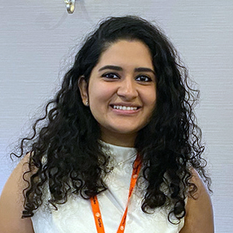 Lasya Aji Silpa is facing forward, smiling, wearing a white shirt. She has long curly dark hair.