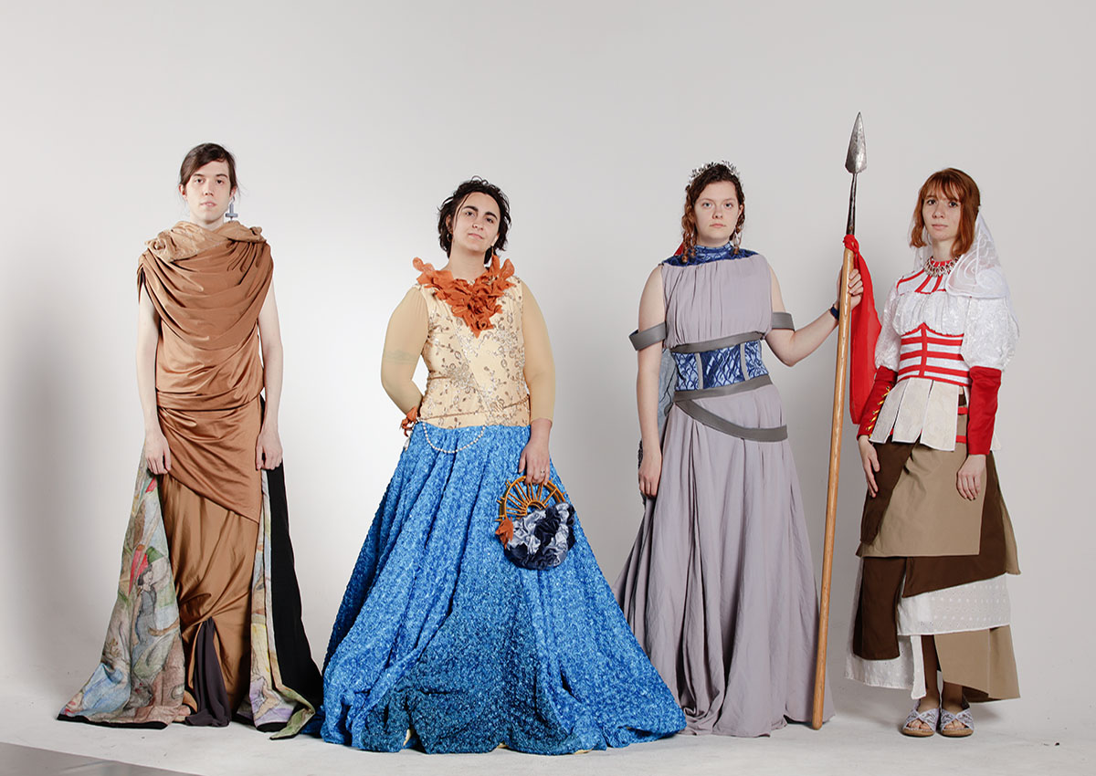 Four models standing in a line wearing big, colorful garments, standing in front of a blank, white background.