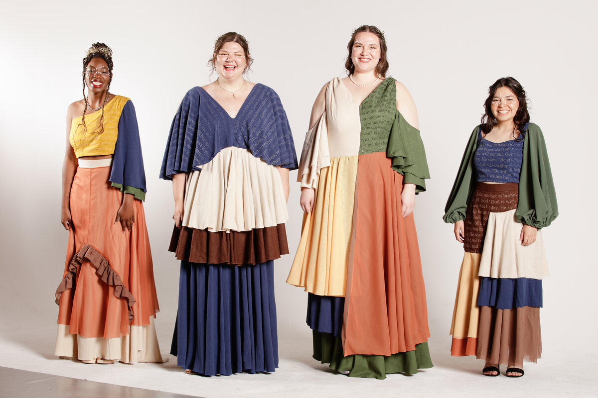 Two models wearing long dresses made of different colored linen, and two models wearing two-piece garments standing in a white studio room. 