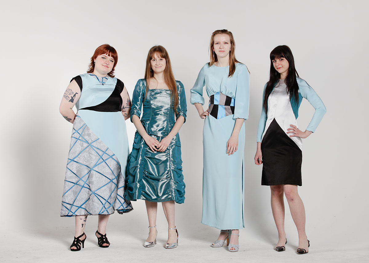 Four models wearing dresses of varying lengths using a mixture of aqua crepe, teal taffeta, black satin, and silver satin in front of a white background.