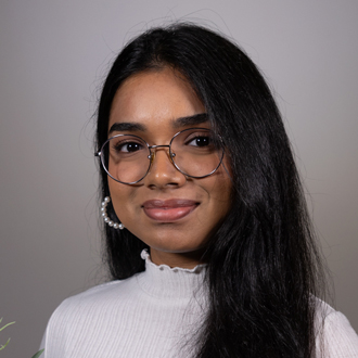 Sadhwika is facing forward and smiling. She has long dark hair and wears a white top.