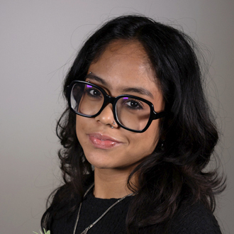 Kaitlyn is facing forward and smiling. She has dark hair and wears glasses.