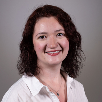 Jillian is facing forward and smiling. She has brown hair and wears a white top.