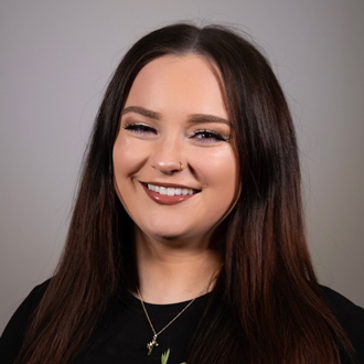Reagan is facing forward and smiling. She has long brown hair and wears a black top.