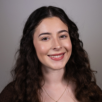 Isabella is facing forward and smiling. She has long, dark, wavy hair.
