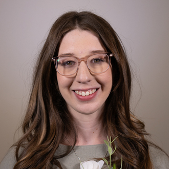 Hannah is facing forward and smiling. She has long blonde hair and wears a green top.