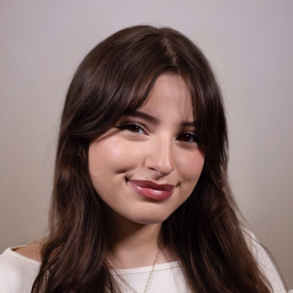 Belen is facing forward and smiling. She has long brown hair and wears a white top.