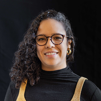 Laura is facing forward and smiling. She has long wavy, dark hair and wears a black top.