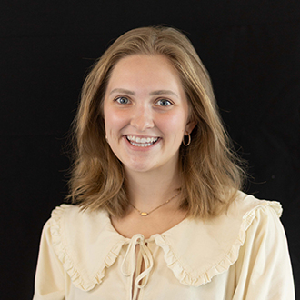 Brooke is facing forward and smiling. She has medium-length, blond hair and wears a cream top.