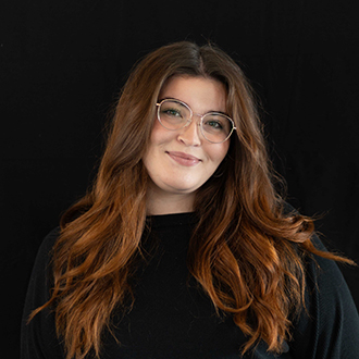 Alexandria is facing forward and smiling. She has long wavy, brown hair and wears a black top.