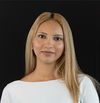 Adilene is facing forward and smiling. She has long blond hair and wears a white top.