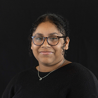 Mia is facing forward and smiling. She has dark hair pulled back and wears a black top.