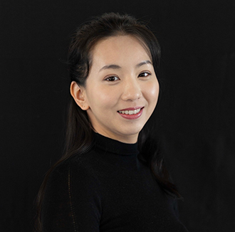 Penney is facing a three-quarter view and smiling. She has long dark hair and wears a black top.