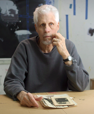 Vernon Fisher facing forward and sitting at a table. He has white hair and wears a gray sweater.