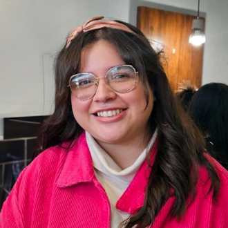 Jazmine is facing forward and smiling. She has long dark hair, wears glasses and hot pink jacket.