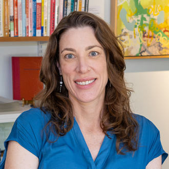 Karen facing forward and smiling. She has long brown, wavy hair and wears a blue top. Bookshelves are in the background.