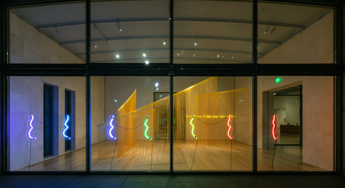 View from outside a window of The Queer Birth exhibit. Neon profiles of women's torsos.