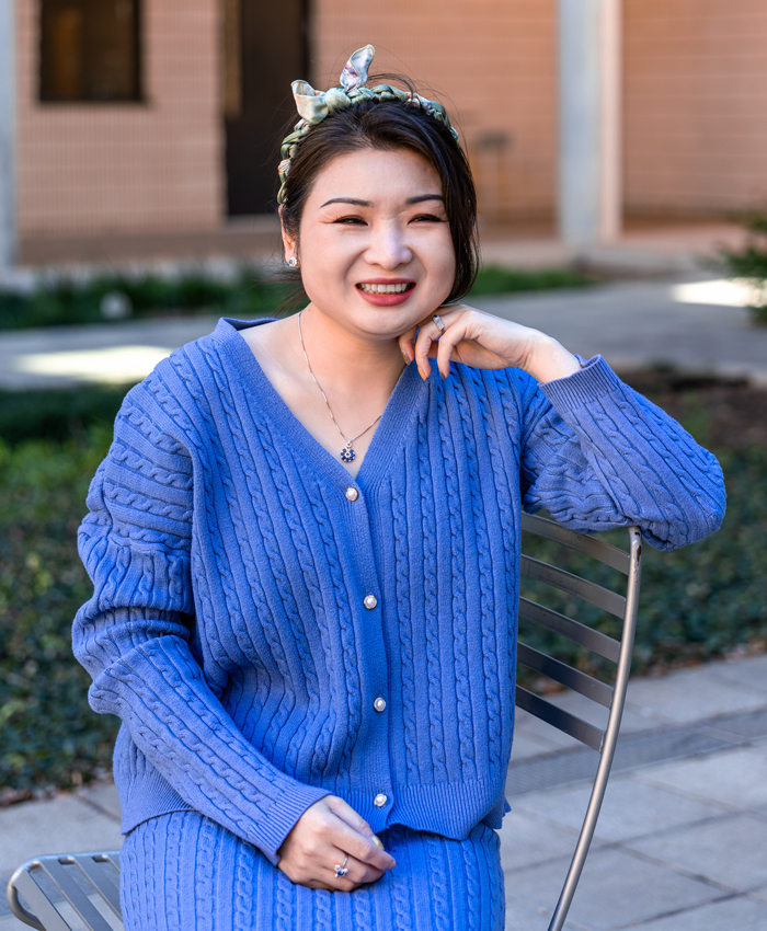 Panpan Yang is facing forward and smiling. She wears a bow in her dark hair and a blue sweater suit.
